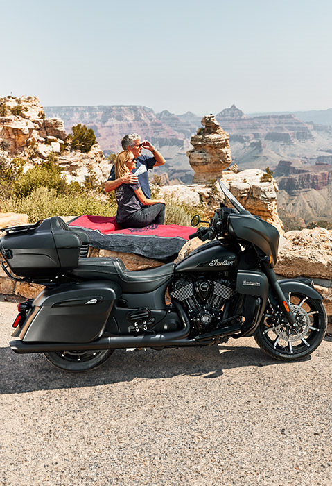2 people sitting on rocks overlooking a canyon behind their 2026 Indian Roadmaster Dark Horse touring motorcycle in the black smoke colorway.