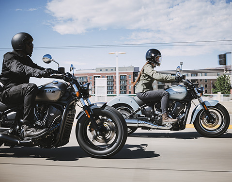2 2025 Indian Scout Sixty Classic motorcycles cruising down a city street.