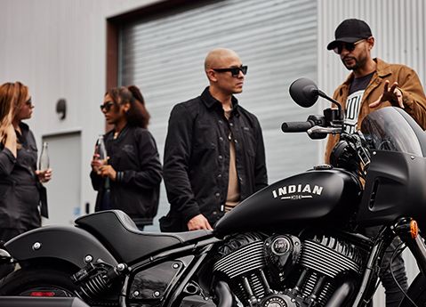 2 men talking near a Black Smoke 2025 Indian Sport Chief motorcycle. 