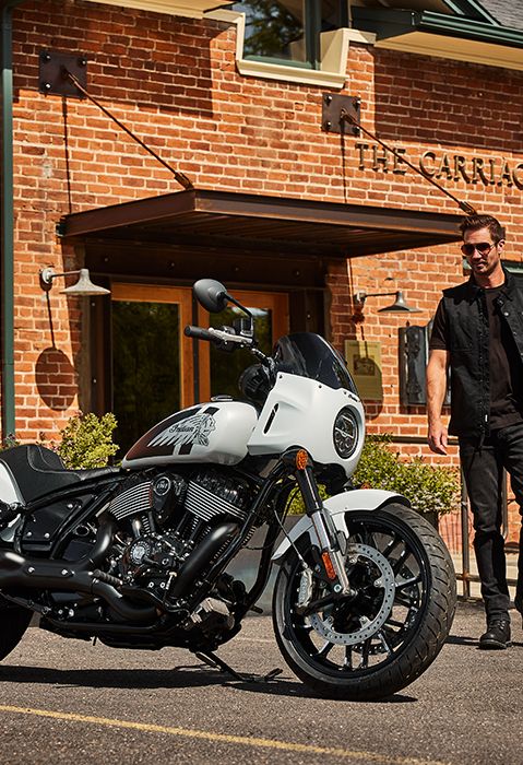 A man walking towards a parked 2025 Indian Sport Chief motorcycle in the Ghost White Metallic Smoke colorway.
