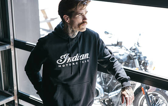 Man leans against window while wearing a black Indian Motorcycle hoodie. 