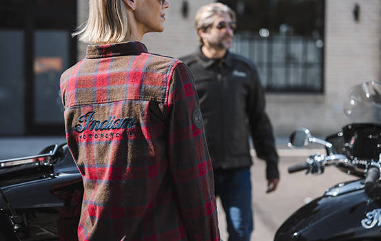 Woman in Indian Motorcycle flannel greeting man in leather Indian Motorcycle jacket. 