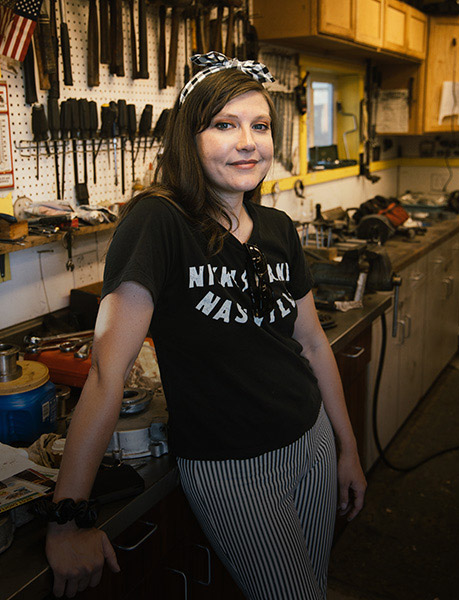Indian Scout Motorcycle Builder, Brittney Olsen, smiles in mechanic shop. 