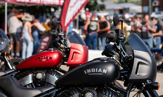 Attendees admiring custom black Indian Motorcycle at Sturgis Motorcycle Rally event, family and bikes enthusiasts present.
