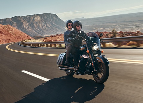 A man and a woman riding on an Indian Chief vintage cruiser motorcycle down the highway.