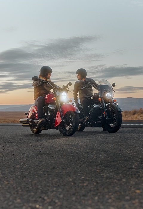 2 people chatting while sitting on their Indian Chief vintage cruiser motorcycles.