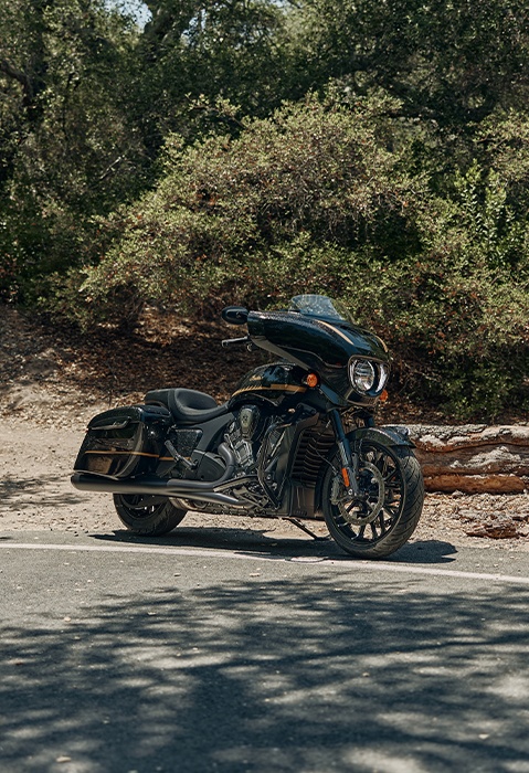 An Indian Chieftain PowerPlus bagger motorcycle parked in a lot near a hiking trail by a forest.