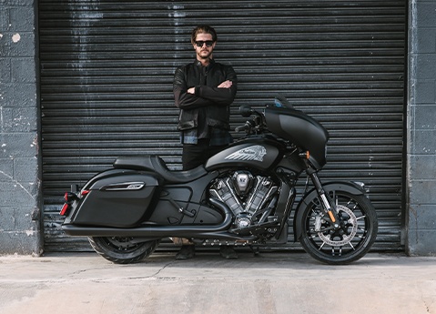 A man standing behind a Indian Chieftain PowerPlus bagger motorcycle in front of a garage.