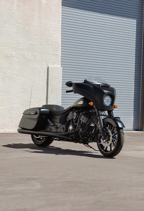An Indian Chieftain bagger motorcycle in the black smoke colorway parked in front of a garage.