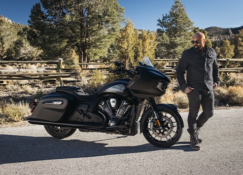 A man walking around an Indian Challenger Dark Horse motorcycle.