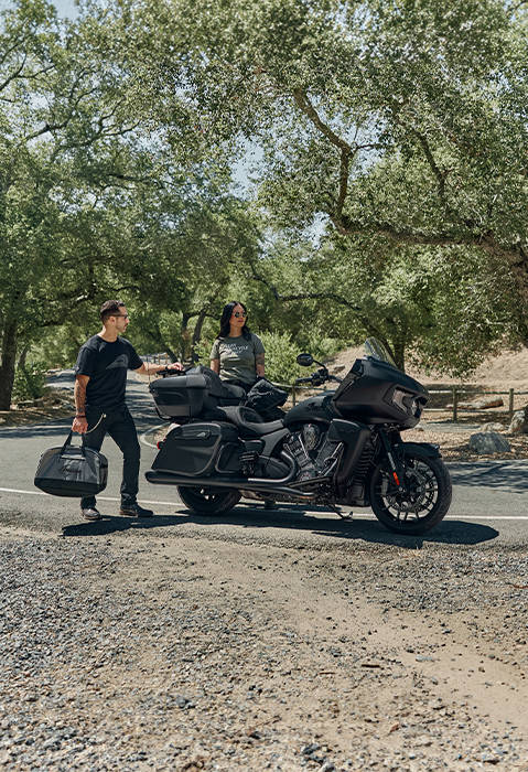 2 people standing behind an Indian Pursuit Dark Horse touring motorcycle.