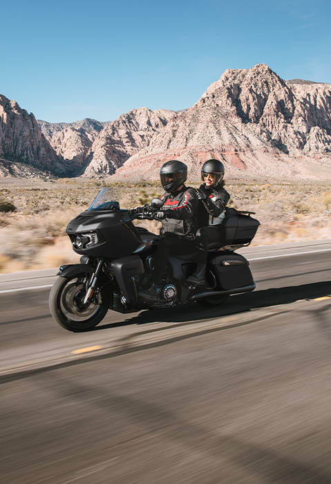 2 people with helmets on riding a Indian Pursuit Dark Horse touring motorcycle on the highway.