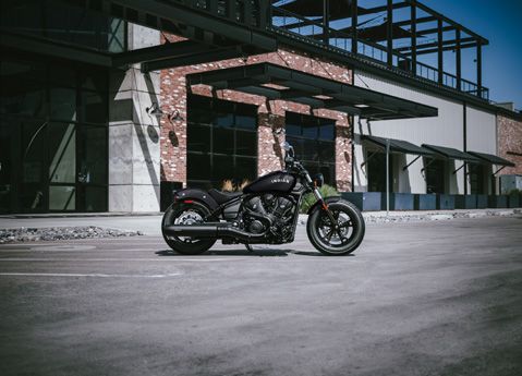 Side profile of an Indian Scout Sixty mid-size cruiser motorcycle parked in front of a modern building.