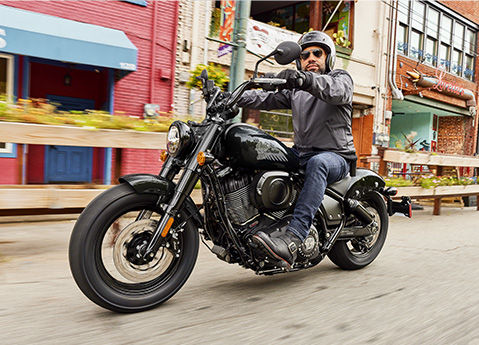 A man riding a 2026 Indian Chief Bobber Dark Horse cruiser motorcycle down a city street.