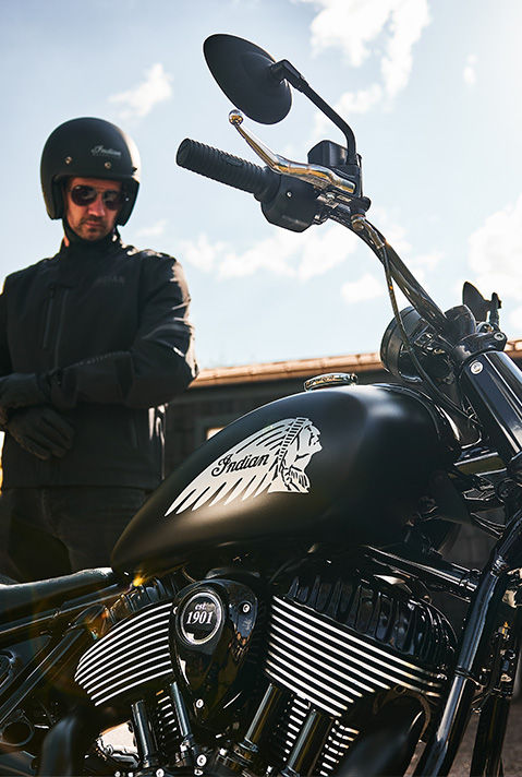 A man putting his gloves on and preparing to ride his 2026 Indian Chief Bobber Dark Horse cruiser motorcycle.