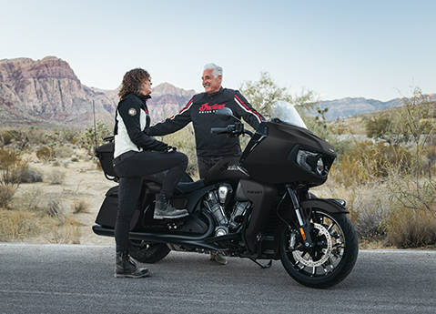 A man and a woman smiling at each other after a ride on their 2-seater 2026 Indian Pursuit Dark Horse touring motorcycle.