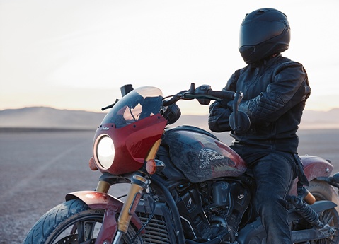 A rider with their arms crossed sitting on a 2026 Indian 101 Scout cruiser motorcycle in the desert.