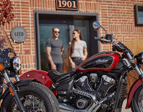 2 people standing behind a 2026 Indian Scout Classic cruiser motorcycle.