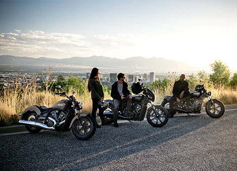 3 people chatting near their 2026 Indian Scout Sixty Classic cruiser motorcycles.