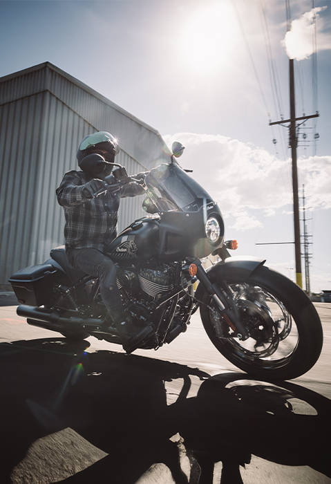 A person riding a 2026 Indian Sport Chief RT cruiser motorcycle down a city street.