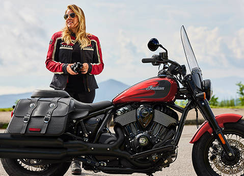 Una mujer de pie detrás de una motocicleta 2026 Indian Super Chief Dark Horse en el esquema de color Sunset Red Metallic.
