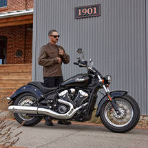 A man zipping up his jacket before riding an Indian Cruiser motorcycle. 