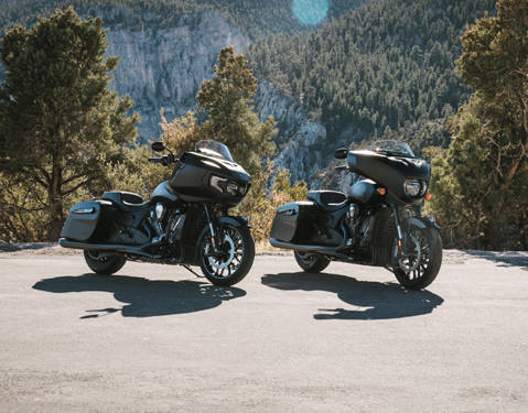 2 Dark Horse blacked-out Indian motorcycles parked with a forest in the background.