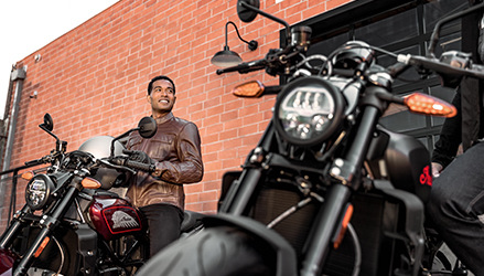 A man wearing an Indian apparel motorcycle jacket, standing near his motorcycle