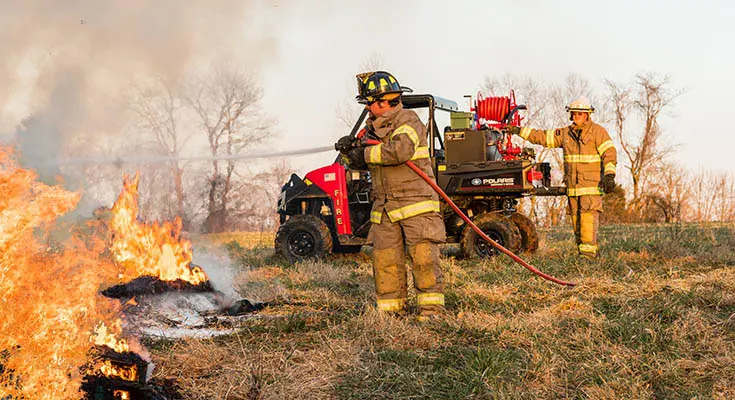 fire fighter spraying a fire with a hose connected to polaris ranger UTV