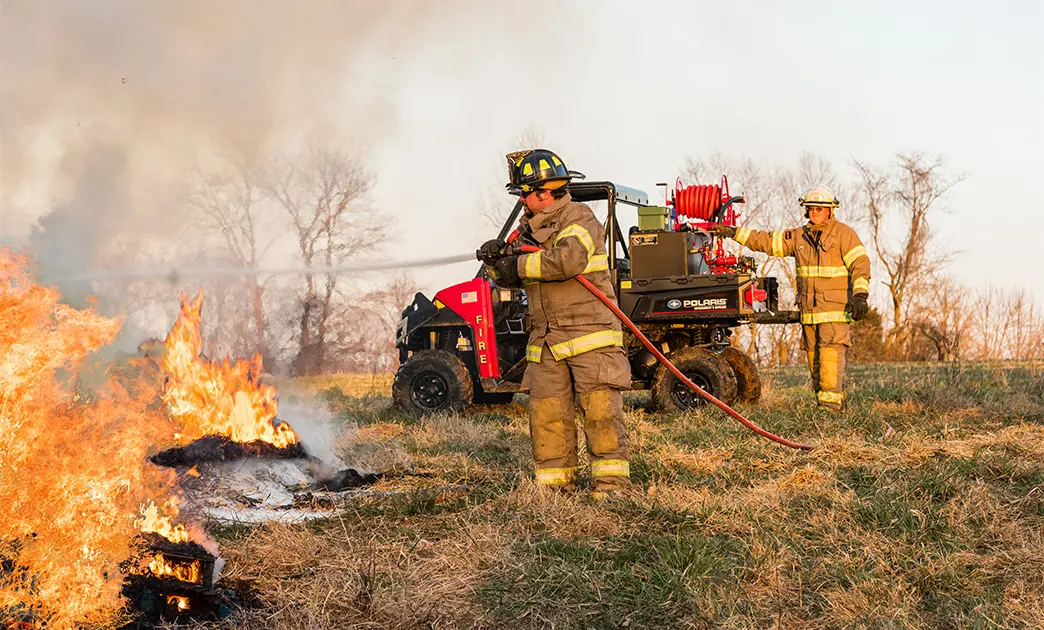 fire fighter spraying a fire with a hose connected to polaris ranger UTV