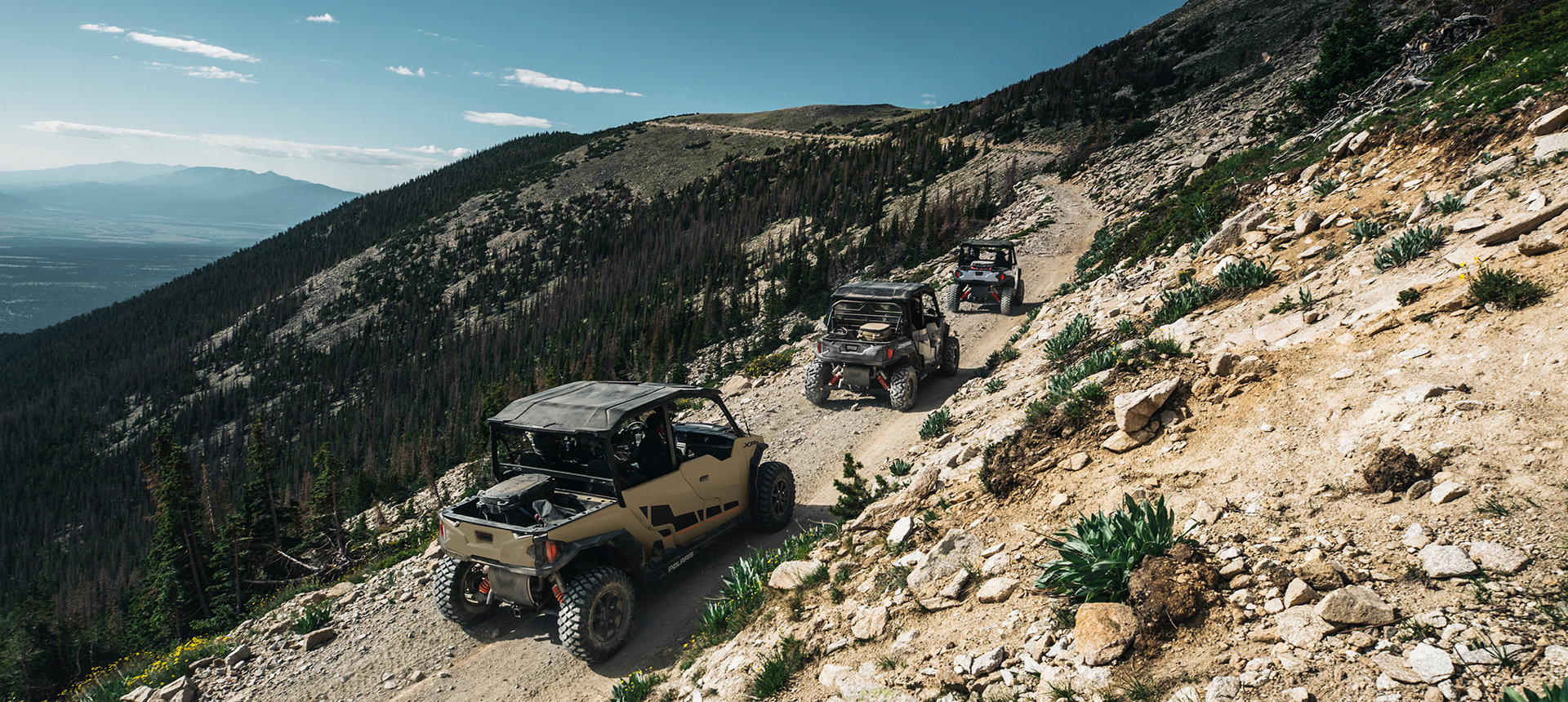 Three General vehicles following each other through a trail in the mountains