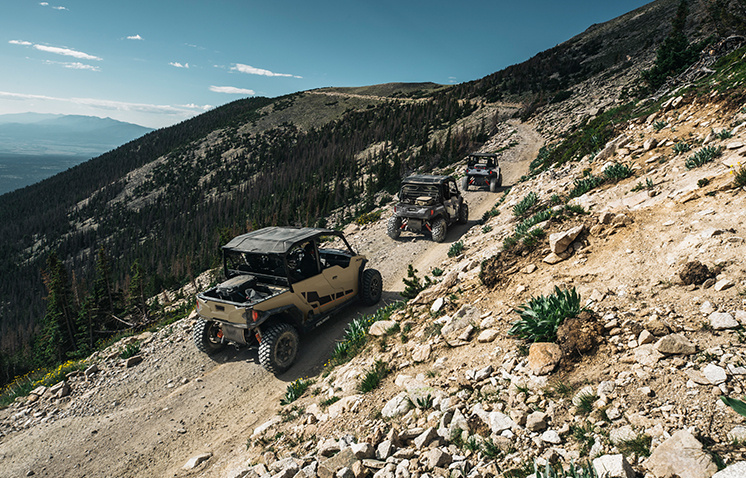 Three General vehicles following each other through a trail in the mountains
