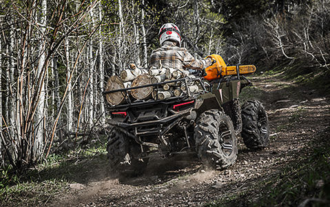 polaris sportsman xp 1000 atv driving down a forest trail with racks fully loaded with wood and a chainsaw