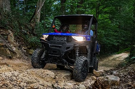 2 riders in a ranger sp 570 utv with headlights on in a forest
