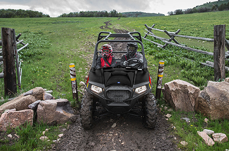 2 riders in a rzr trail 570 going through a narrow gate