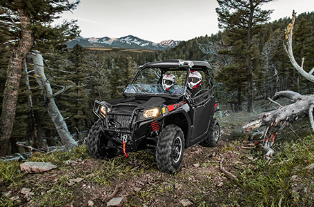 2 riders in a rzr trail 570 driving down a forest trail