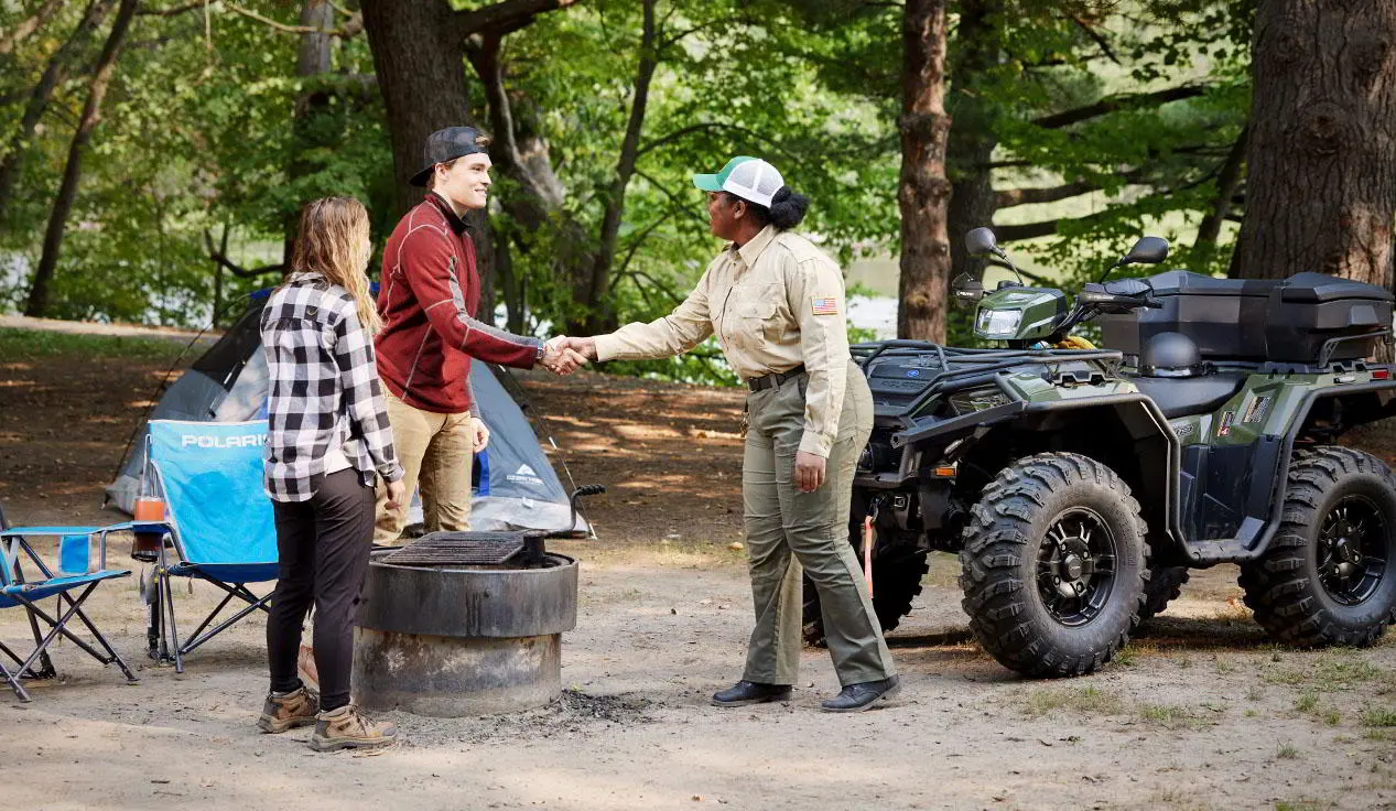 Government Official shaking hands with a camper near her Polaris Sportsman ATV with terrain and wildlife management package.