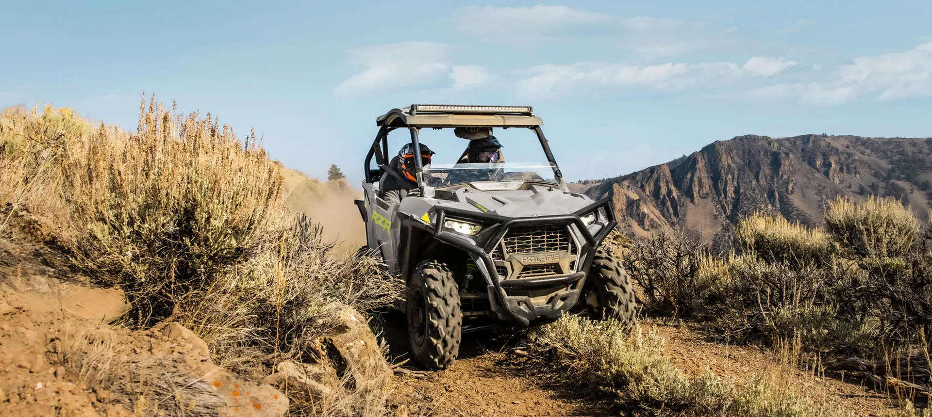 2 riders in a rzr trail side by side driving down a dusty trail