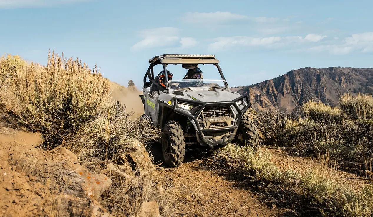 2 riders in a rzr trail side by side driving down a dusty trail