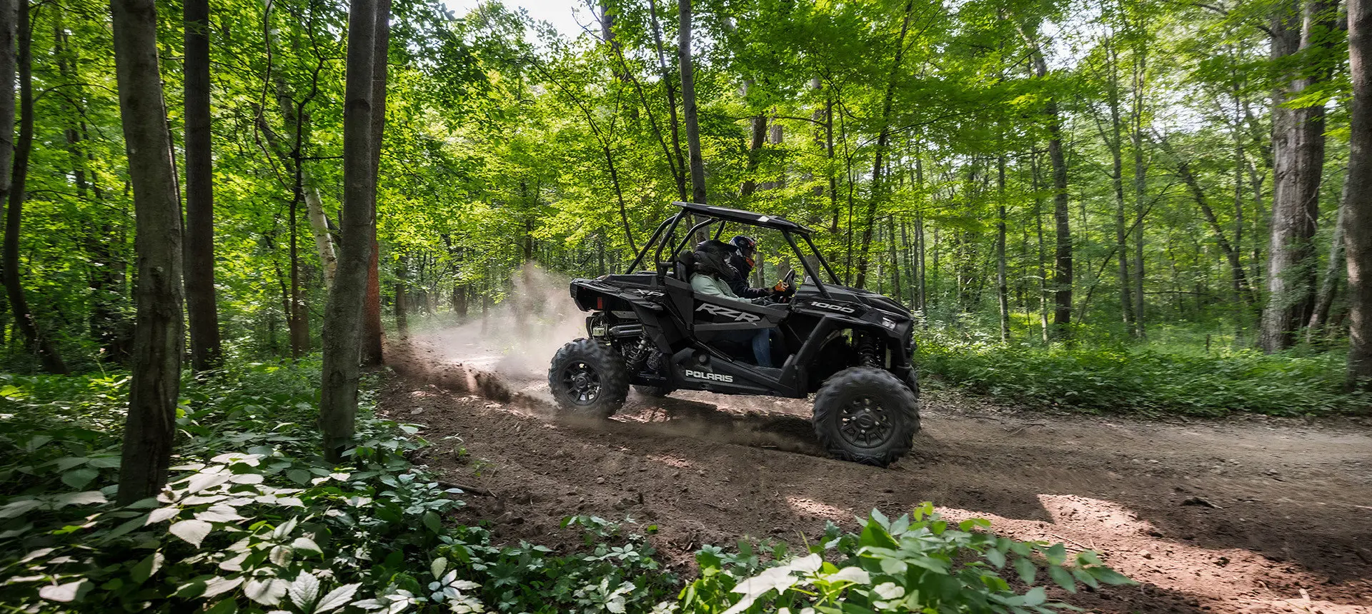 2 riders in a rzr xp 1000 side by side on a forest trail