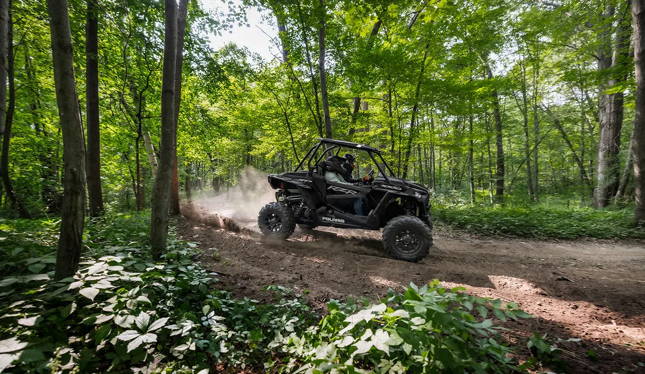 2 riders in a rzr xp 1000 side by side on a forest trail
