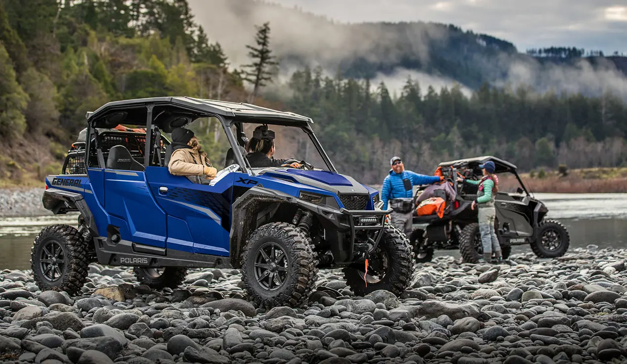 people hanging out in and around their general xp 4 1000 side by sides near a river