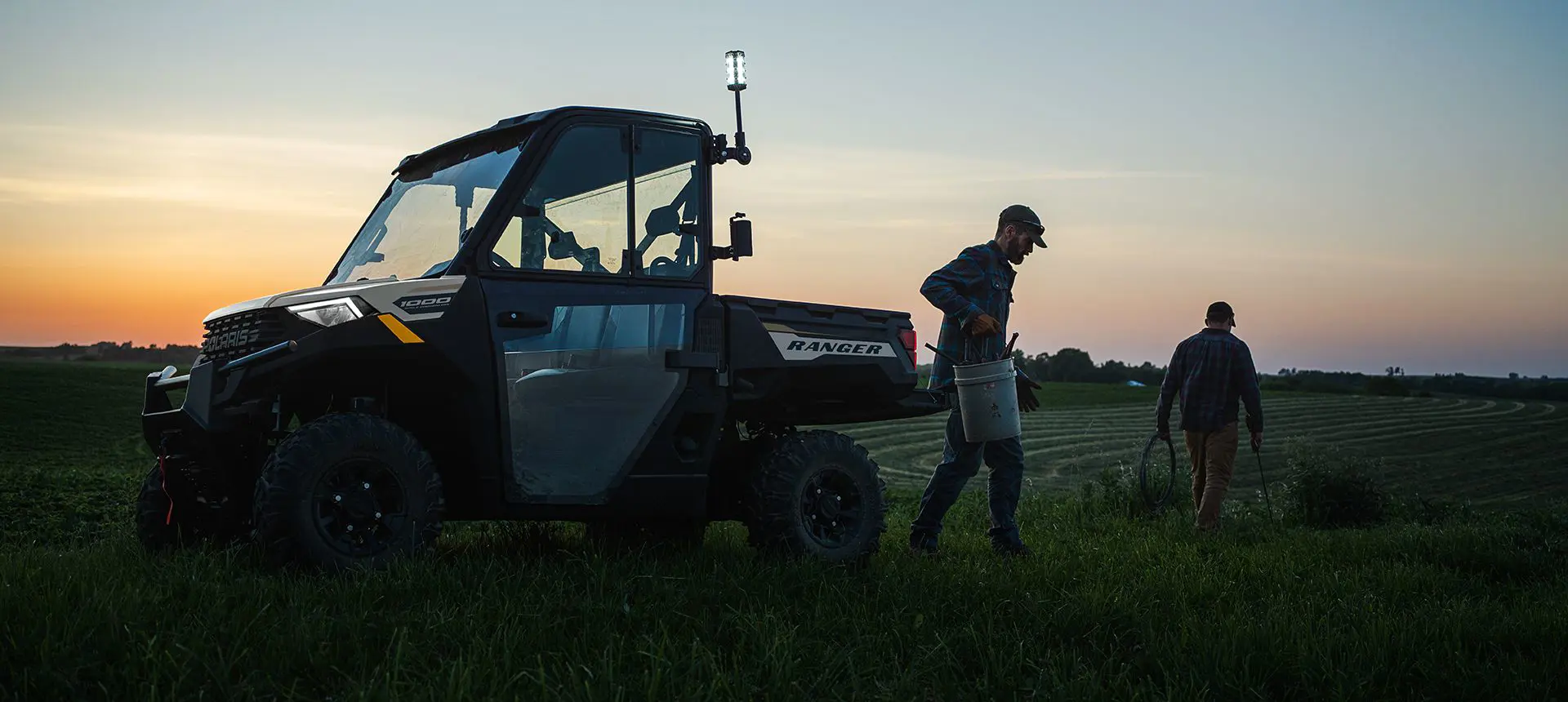 2 farmers grabbing gear to fix a fence from the cargo box of their Polaris RANGER 1000 UTV.