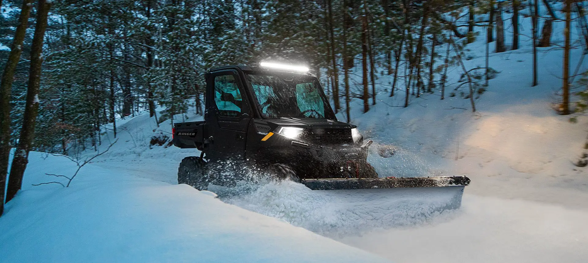 Polaris RANGER 1000 UTV with plow system and door accessories plowing snow at dusk.