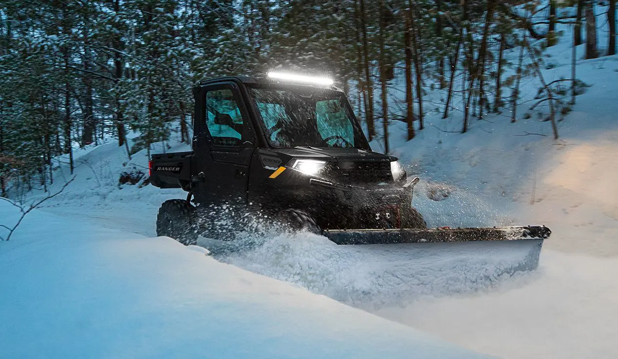 Polaris RANGER 1000 UTV with plow system and door accessories plowing snow at dusk.