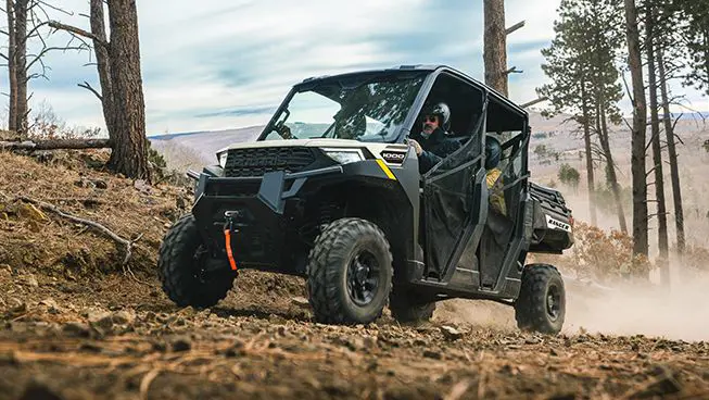 Four people in a Polaris RANGER CREW 1000 UTV driving down a dusty trail.
