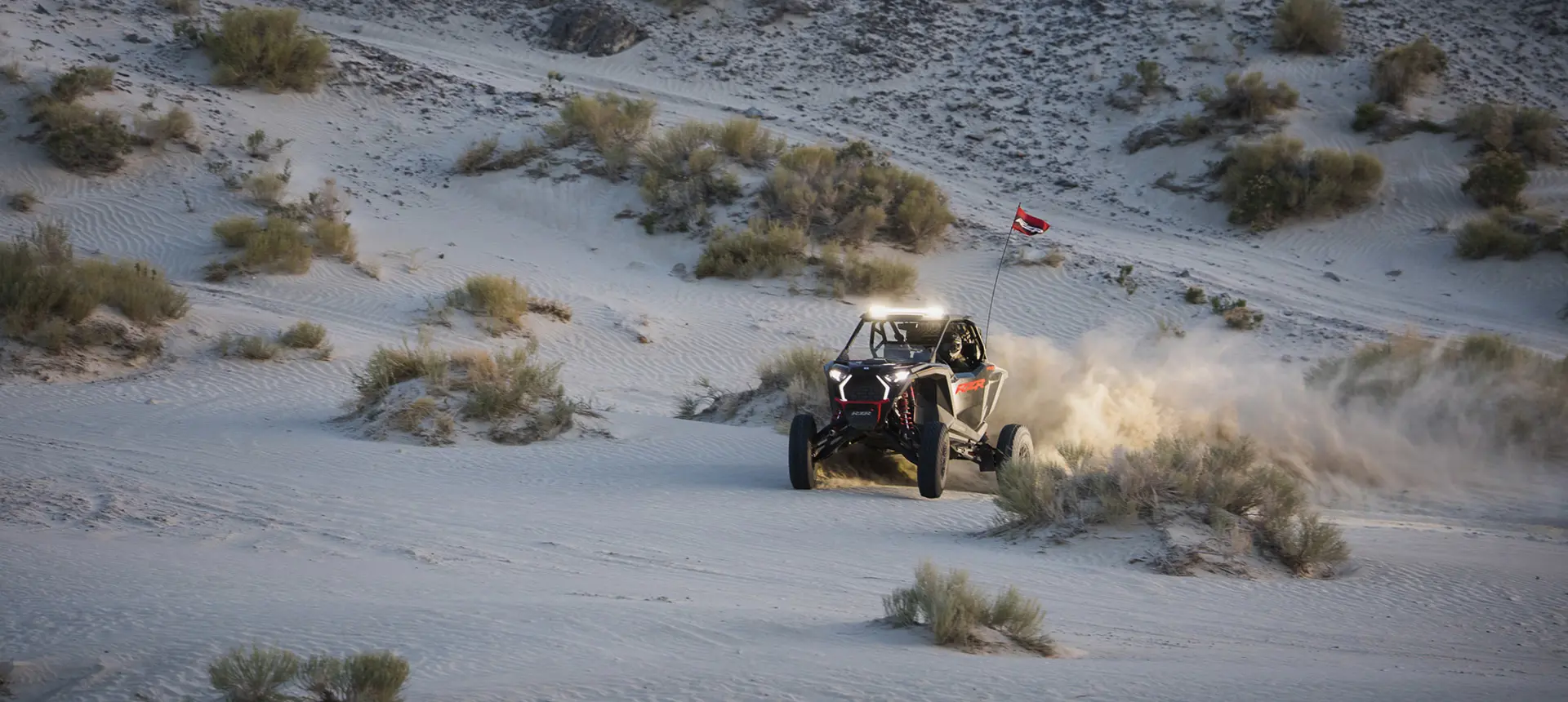 Polaris RZR Pro S side-by-side with headlights illuminated and driving through the desert at dusk.