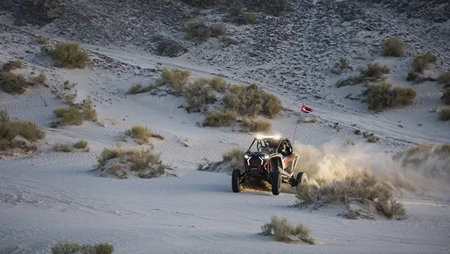 Polaris RZR Pro S side-by-side with headlights illuminated and driving through the desert at dusk.