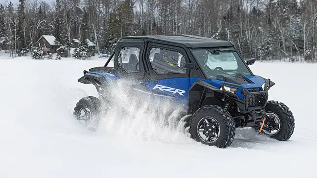 Polaris RZR XP 4 side-by-side driving through a snowy field.