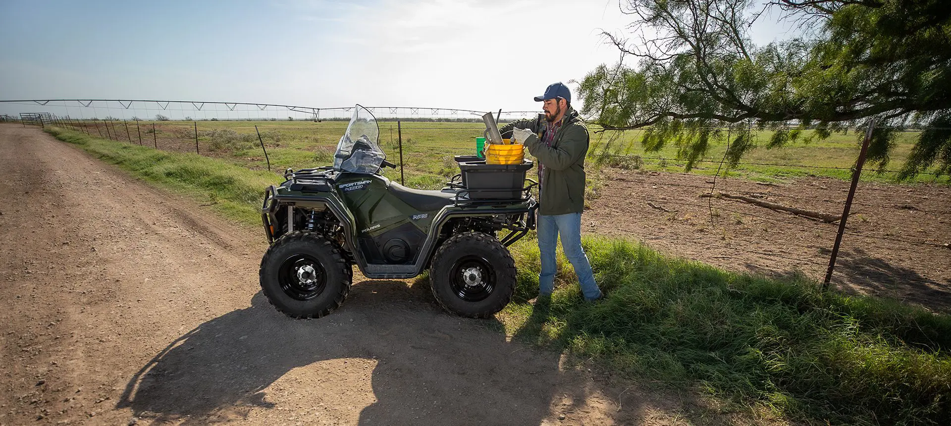 Farmer using the cargo rack on a Polaris Sportsman 450 ATV to haul fencing materials.